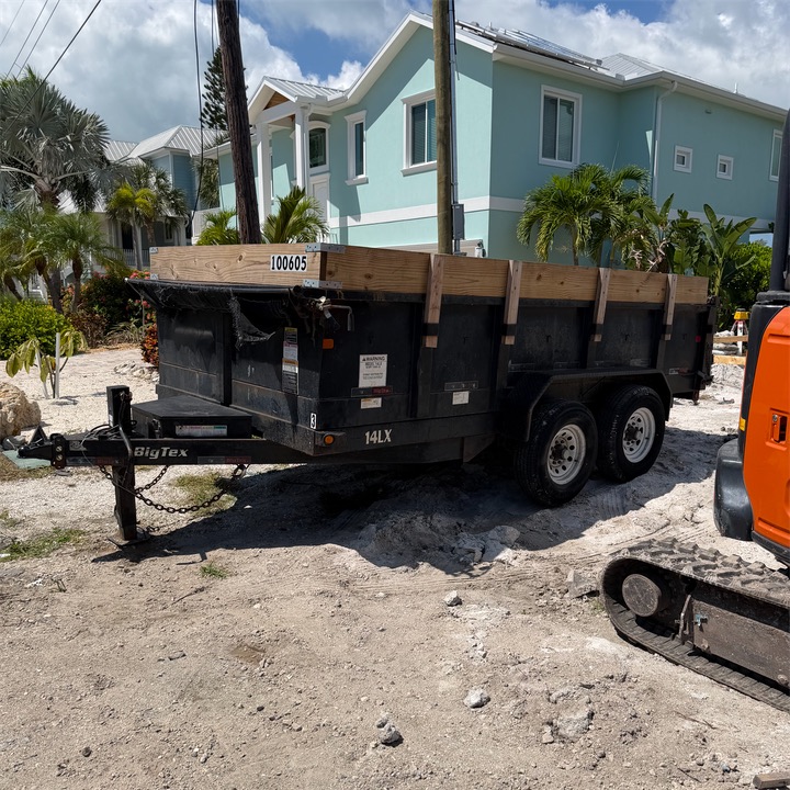 Dump trailer with wood side boards at a job site beside a mini excavator